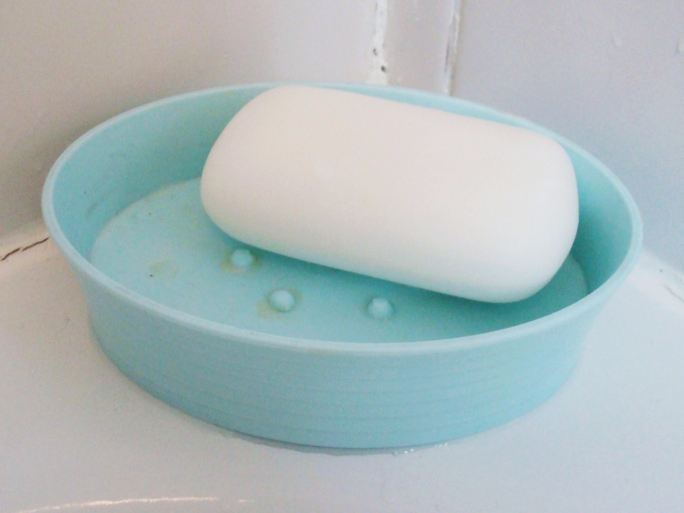 A plain white bar of soap in a light blue plastic soap dish