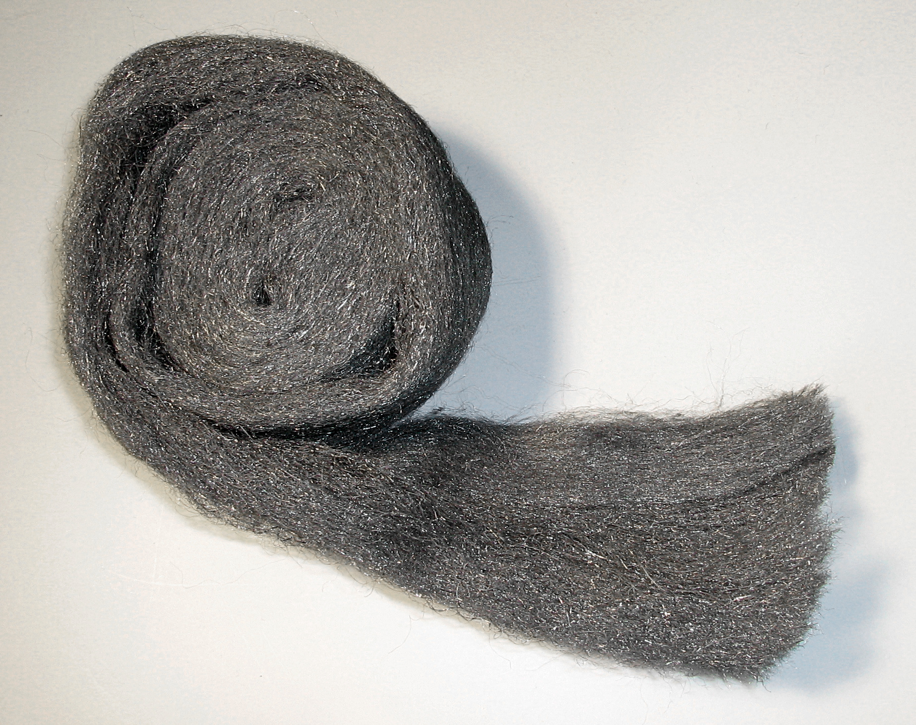 A loose roll of gray steel wool on a white surface
