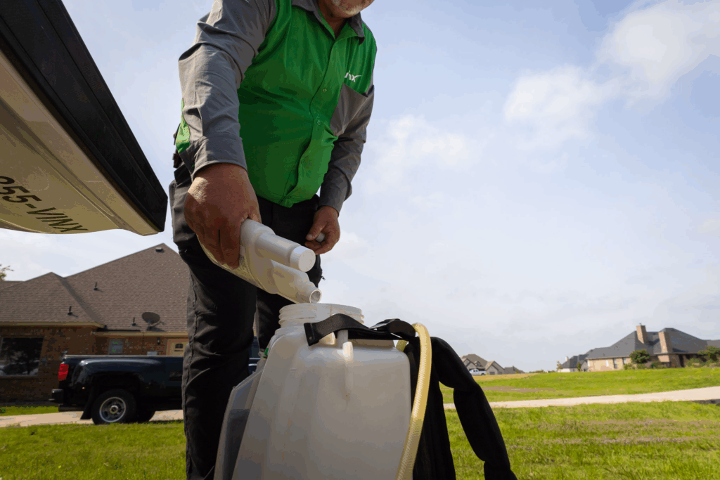 This image shows a pest control technician from Vinx Pest Control wearing a branded uniform while pouring a chemical solution into a sprayer tank. It's a good representation of professionalism, preparedness, and safety practices in residential pest control services.